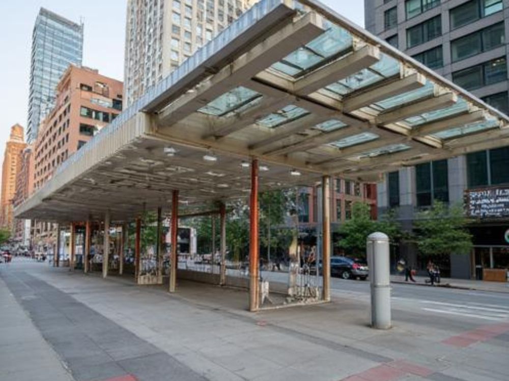 Estrutura urbana com cobertura metálica e pilares em área pública, integrada ao entorno de prédios comerciais e circulação de pedestres.